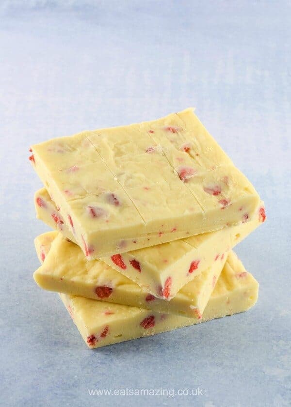 Square blocks of homemade white chocolate fudge with strawberry pieces on a blue shaded background