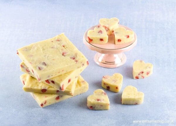 Strawberries and Cream White Chocolate Fudge blocks and heart shaped fudge on a mini pink cake stand against a pale blue background