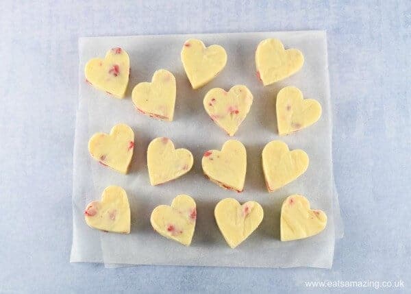 Strawberries and Cream White Chocolate Fudge cut into heart shapes on a folded piece of baking paper with a light blue background