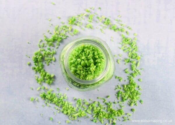 Green homemade coconut sprinkles in a glass jar with sprinkles scattered around