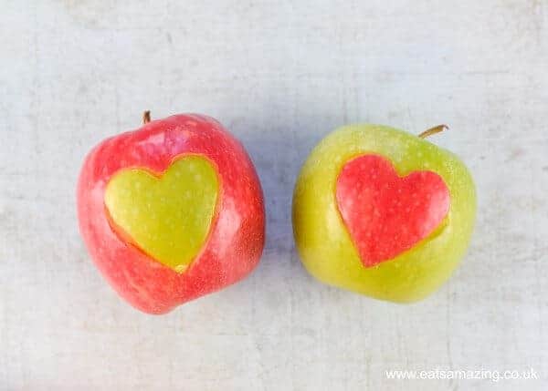 Shiny pink and green Apples with hearts cut into the skin and swapped - side by side on a grey green backdrop