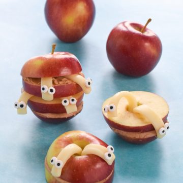Sliced apple snack with peanut butter and cheese worms with plain apples in the background