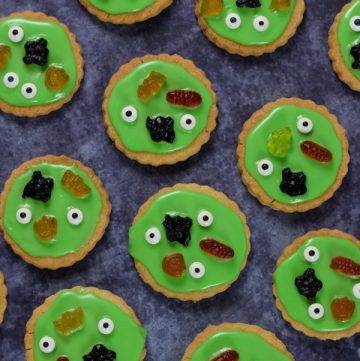Swamp monster cookies topped with green icing and halloween sweets on a dark backgrond