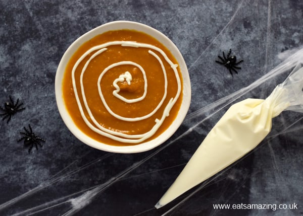 pumpkin soup with spiral of yogurt piped on top - yogurt in a piping bag on the side