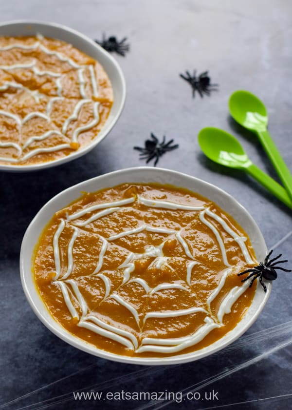 Pumpkin soup in white bowls with yogurt spider web topping and green spoons on a dark background